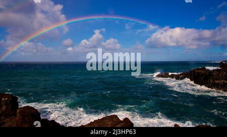 Canary Islands, Lanzarote, volcanic island, southwest coast, rugged volcanic coast, strong surf, sea caves, view of a rainbow over the sea, sea dark green, sky blue and clear, clouds gray and white Stock Photo