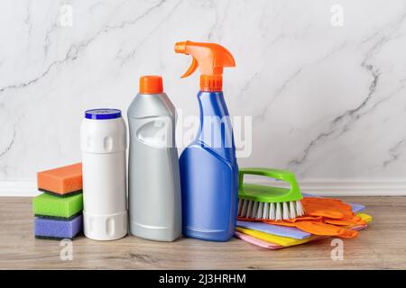 Domestic cleaning supplies on the wooden shelf against marble wall. Cleaning powder, liquid detergent, spray bottle, sponges, gloves and brush. Stock Photo