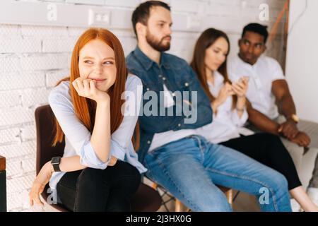 Portrait of happy female job candidates smiling looking away while waiting interview sitting in queue line row with diverse multi-ethnic candidates. Stock Photo