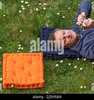 A man is lying in a meadow with his head on a square pillow and another square pillow next to it Stock Photo