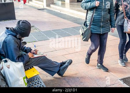A young man sitting on a bench writing in his notebook in the street. Winter Madrid, Spain Stock Photo