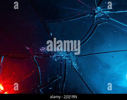Close-up photo texture of blue and red toned broken and cracked glass on black backdrop. Stock Photo
