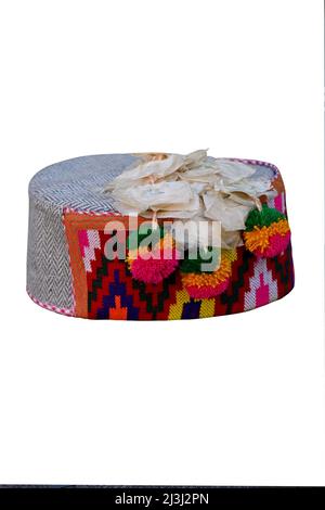 closeup the colorful hand made himachali indian traditional cap with hanging white flowers isolated on white background. Stock Photo