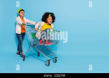 Full length body size view of small little friends friendship riding cart having fun isolated over bright blue color background Stock Photo