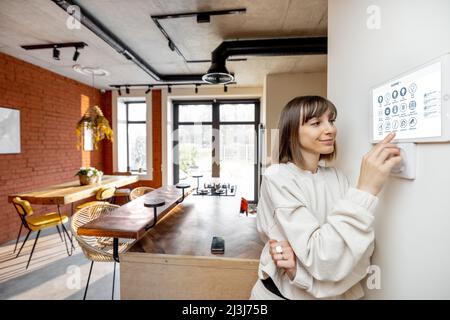 Woman controlling home devices with digital smart panel mounted on the wall Stock Photo