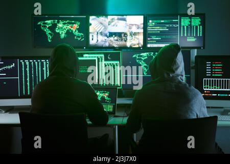 Control room monitoring surveillance video camera control city - Two Hooded hackers in dark room office full device from secret service public safety Stock Photo