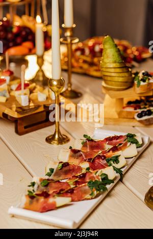 Prosciutto with pear and basil on a black stone plate. Jamon. Italian antipasto. Top view.Catering Stock Photo