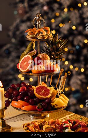 beautiful ripe tangerines lie in a plate on the table close-up with blurred background on the background of a Christmas tree decorated with garlands a Stock Photo