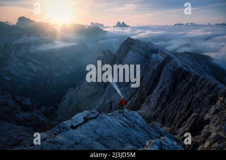 Europe, Italy, Alto Adige - Südtirol, Hiker looking at the landscape towards the Sexten Dolomites from the summit of the Picco di Vallandro / Dürrenstein illuminated by the light of the full moon Stock Photo