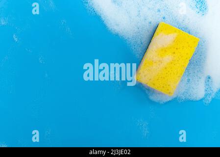 Soap foam. Yellow sponge on a blue background with soapy foam. Place on background for text Stock Photo