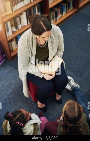 Everyone loves a good story. High angle shot of a teacher reading to a group of elementary school kids in the library. Stock Photo