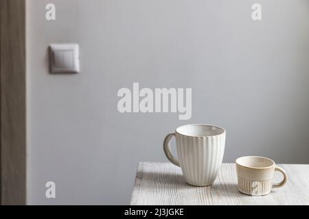 Two porcelain white cups are on the beige table. Large and small cup Stock Photo