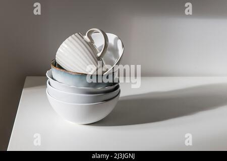 A pyramid of white bowls, plates and cups of different sizes and colors on a beige table in the kitchen. Scandinavian style. Place for your text. Copy Stock Photo