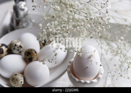 Table decorated for Easter in beige tones. Dried gypsophila, chicken and quail eggs, a silver figurine of a hare and a cup of coffee. Easter concept. Stock Photo