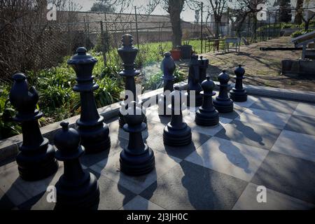 A large outdoor chess set. Here you can see the placement of the black game pieces in the backlight with long shadows. Symbolic image of military stre Stock Photo