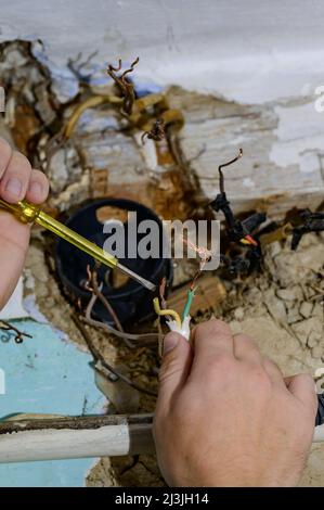 Old electrical wiring in the house, wooden walls in the house, replacement of electrical cables, the master checks the old wire for contact with elect Stock Photo