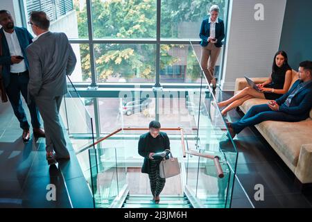 Lets get this day started. Shot of a young businesswoman walking up the stairs while using a digital tablet in a busy office at work. Stock Photo