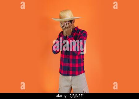 Black Man With Junina Party Outfit  Isolated on Orange Background.  Young man wearing traditional clothes for Festa Junina - Brazilian June festival. Stock Photo