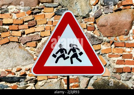 Triangular warning 'children crossing' school road traffic sign with stone masonry wall behind Stock Photo