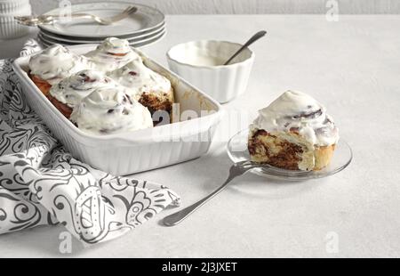 Cinnamon rolls with cream cheese in a baking dish and one lays separate. Seasonal autumn homemade pastry - cinnabons for breakfast or holidays. Stock Photo