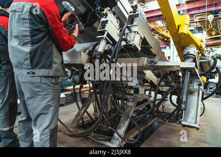 Workers at farm machinery factory assemble spare parts on special machine tool in workplace. Stock Photo