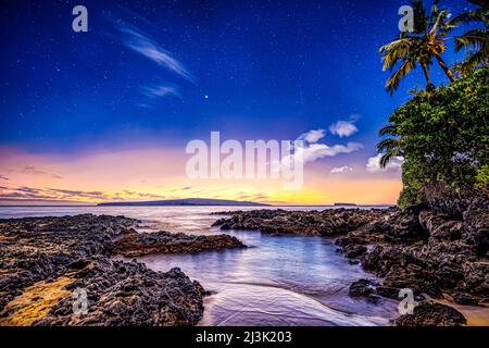 Landscape in a Hawaiian paradise in Makena Cove at sunset with rugged rocks and lush vegetation lining the shoreline, and stars in the clear sky Stock Photo