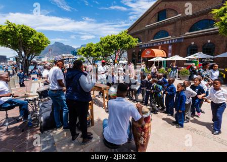 School children in uniform stop to listen to a percussion musical group along the waterfront of Cape Town; Cape Town, South Africa Stock Photo