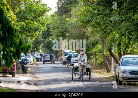 Street scene in a village in India with vehicles and motorcycles, and a man cycling with a trailer and talking on the phone Stock Photo