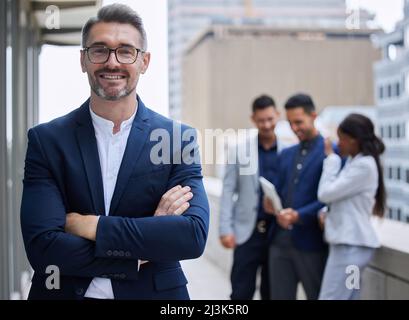 Confident with a great team behind me. Cropped portrait of a handsome mature businessman standing outside with his arms folded with his colleagues in Stock Photo