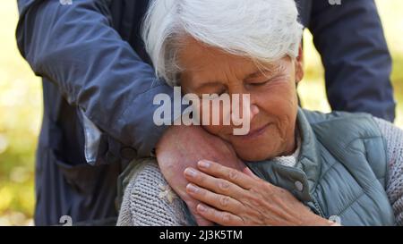 Portrait of elderly Caucasian lady leans to the hand of her husband, man stands behind his wife closing eyes emotional support concept . High quality photo Stock Photo