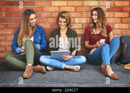 Wifi lets them study anywhere on campus. Shot of three smiling female university students sitting together outside on campus using a digital tablet. Stock Photo