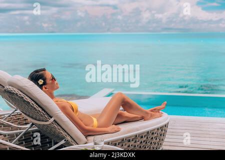 Luxury vacation in paradise Bora Bora high end resort hotel bikini woman relaxing lying on lounger sunbathing by the swimming pool at overwater villa Stock Photo