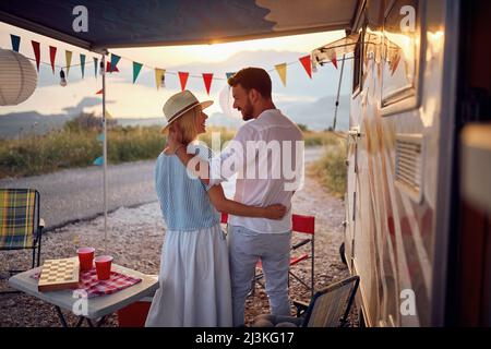Man and woman hugging and looking at each other smiling in front of camper rv in beautiful nature. Fun, togetherness, nature concept. Stock Photo