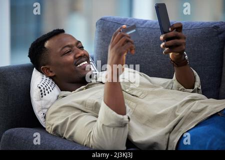 Shopping from the comfort of my couch. Shot of a young man using a credit card and phone on the couch at home. Stock Photo