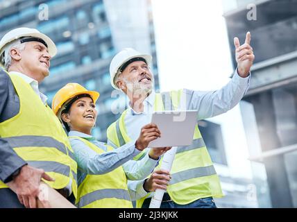Managing a complex project together. Shot of a group of businesspeople using a digital tablet while working at a construction site. Stock Photo