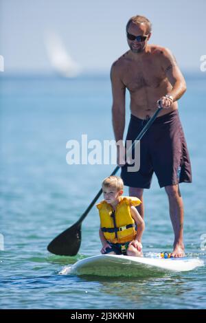 A man paddles his young son around in the waves on a stand up paddleboard. Stock Photo