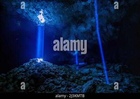 Light rays pass through holes in the cave ceiling in an underwater cave system. Stock Photo