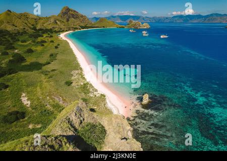 Aerial view of a white sand beach along the shore of Padar Island in Komodo National Park with boats moored off the shore