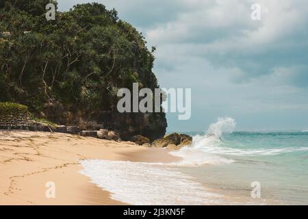 Waves crashing against the rocks with the surf rolling onto the sand at Geger Beach in the Nusa Dua resort area; Geger Beach, Badung, Bali, Indonesia Stock Photo