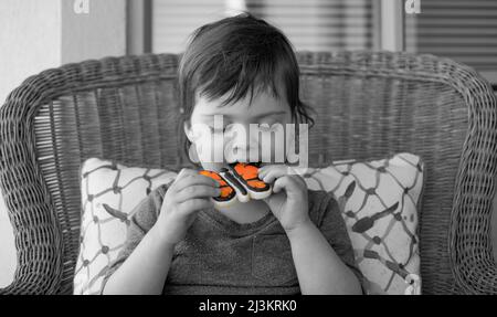 Young girl sitting and eating an iced cookie shaped like a butterfly, with only the butterfly in colour; Surrey, British Columbia, Canada Stock Photo