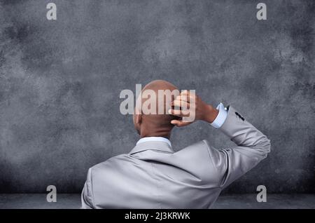 Everything is up in the air. Rearview shot of a businessman scratching his head while looking at a chalkboard. Stock Photo
