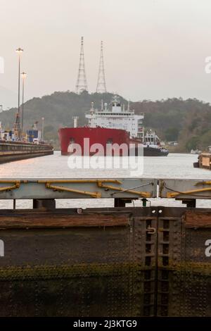 A large shipping vessel is positioned and guided by a tugboat into the Pedro Miguel Locks of the Panama Canal in Panama Stock Photo