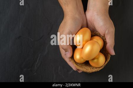 Man hold gloden eggs in bird nest on black background, top view Stock Photo