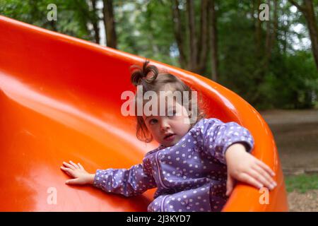 Preschool girl at a playground going down a red slide; North Vancouver, British Columbia, Canada Stock Photo