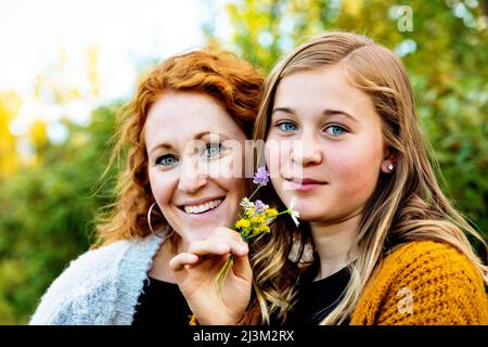 Outdoor portrait of a mother with her teenage girl holding a small cluster of colourful wildflowers and looking at the camera