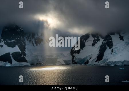 Early morning sun breaking through cloud cover in Antarctica's Lemaire Channel; Antarctica Stock Photo