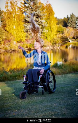 Young paraplegic woman in her wheelchair in a park on a beautiful fall day, feeling carefree with her long hair flipping upwards Stock Photo