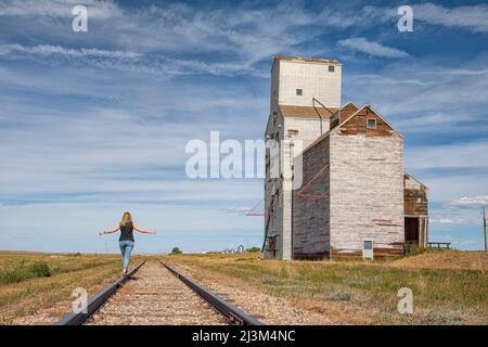 Woman walking on the railway tracks near an abandoned grain elevator in the ghost town of Sanctuary, Saskatchewan; Sanctuary, Saskatchewan, Canada Stock Photo