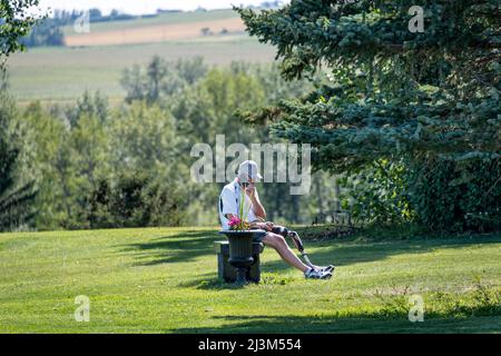 Man with prosthetic leg sits on a bench enjoying time in a park while using his cellphone; Okotoks, Alberta, Canada Stock Photo