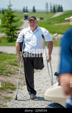 Man with amputated leg stands with crutches on a gravel path on a golf course, looking at the camera; Okotoks, Alberta, Canada Stock Photo